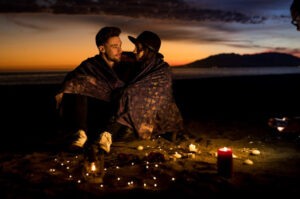 A picture of a young couple in blanket sitting on sea shore